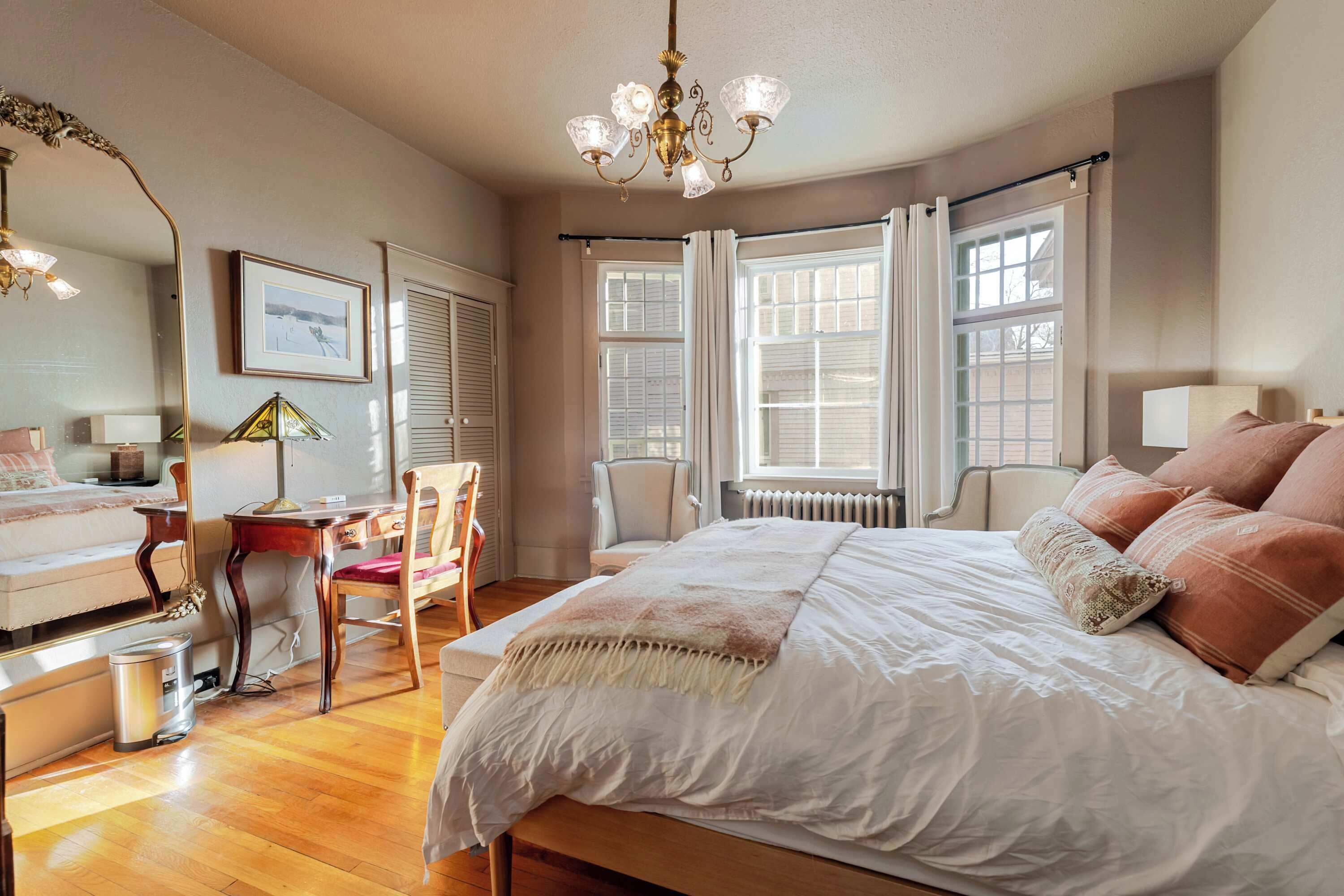 A bedroom with a large bed, a desk, a chair, and a radiator.
