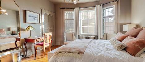 A bedroom with a large bed, a desk, a chair, and a radiator.