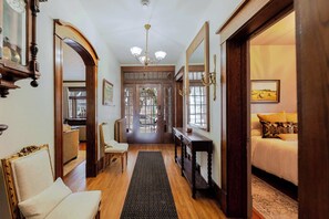 A hallway with wooden flooring, a dark rug, a wooden console table, and a bed with yellow pillows.