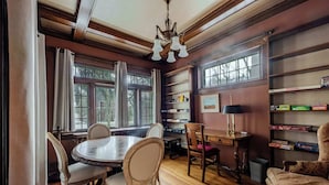 Un coin repas avec une table ronde, des chaises et un lustre. On y trouve également des étagères remplies de livres et une lampe posée sur une table d’appoint.