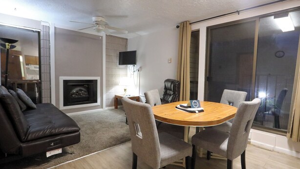 A living room with a fireplace, a round wooden table with chairs, a sofa, and a TV mounted on the wall. - Adorable 1-bedroom condo - 201 Lava Hot Springs Resort (Lava Hot Springs)