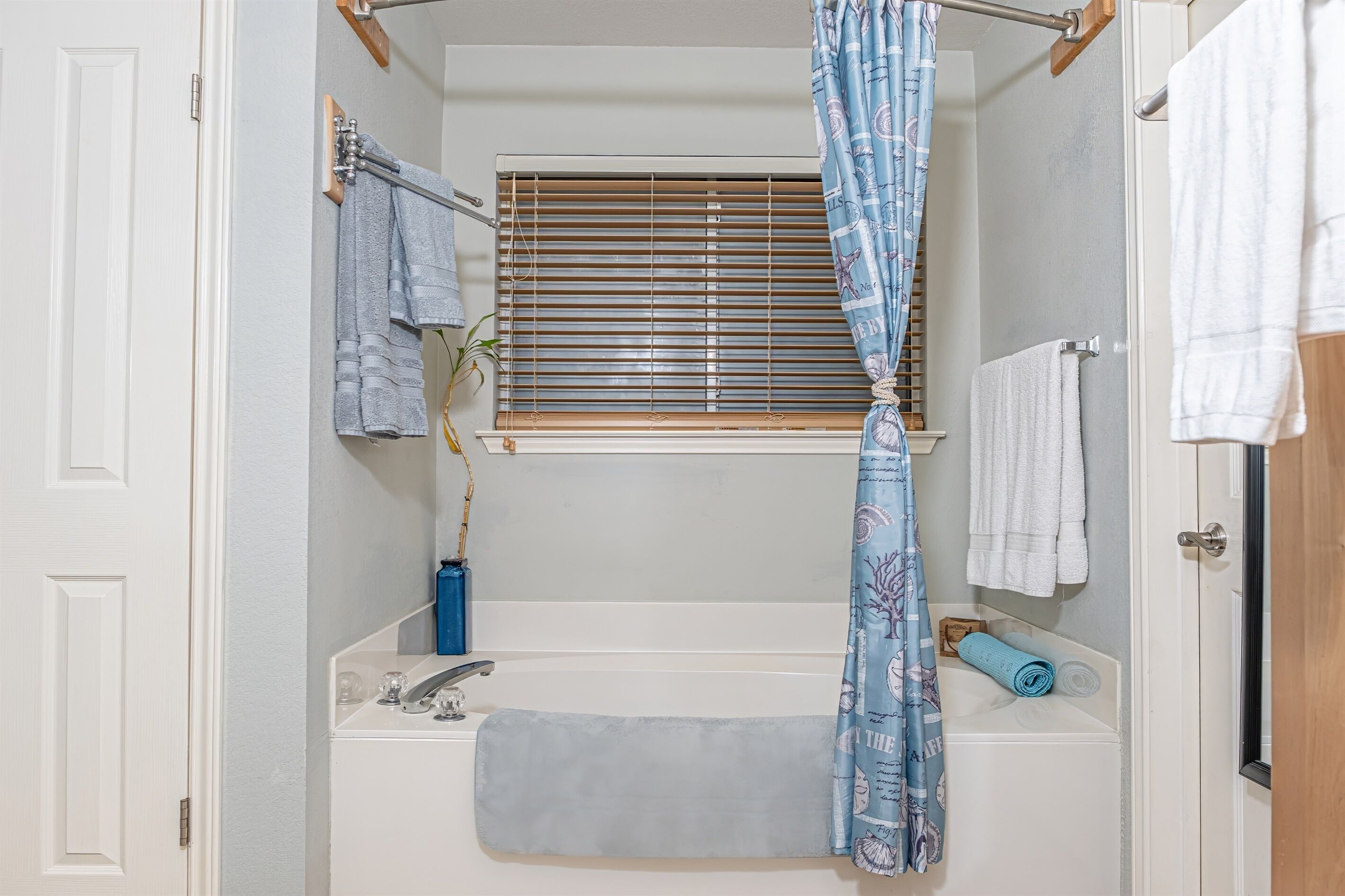 A bathroom with a bathtub, a window with blinds, a towel rack, and a shower curtain.