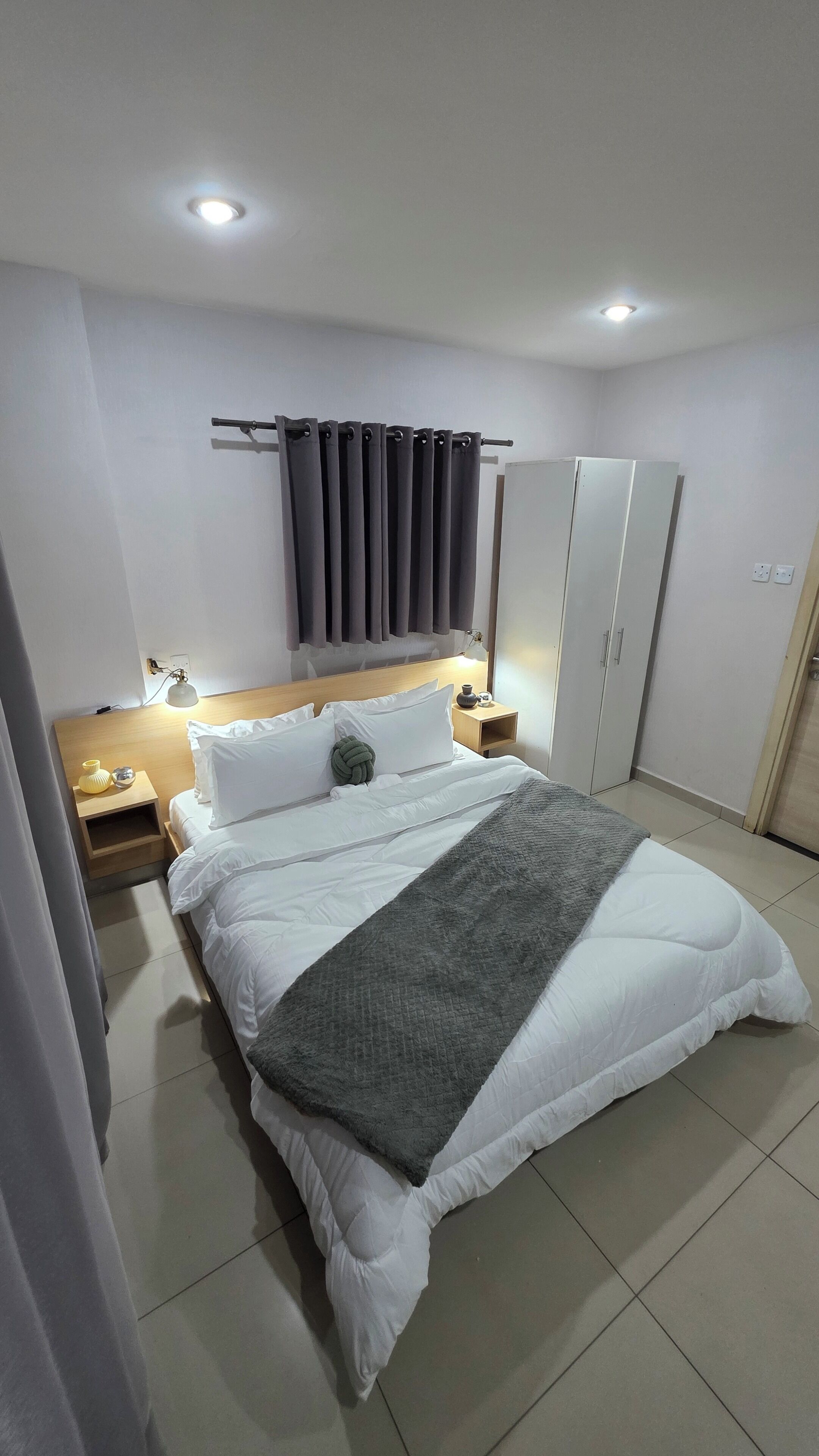 A modern bedroom with a large bed, a nightstand, a wardrobe, and a ceiling light.