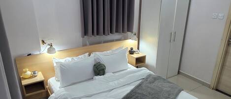 A modern bedroom with a large bed, a nightstand, a wardrobe, and a ceiling light.