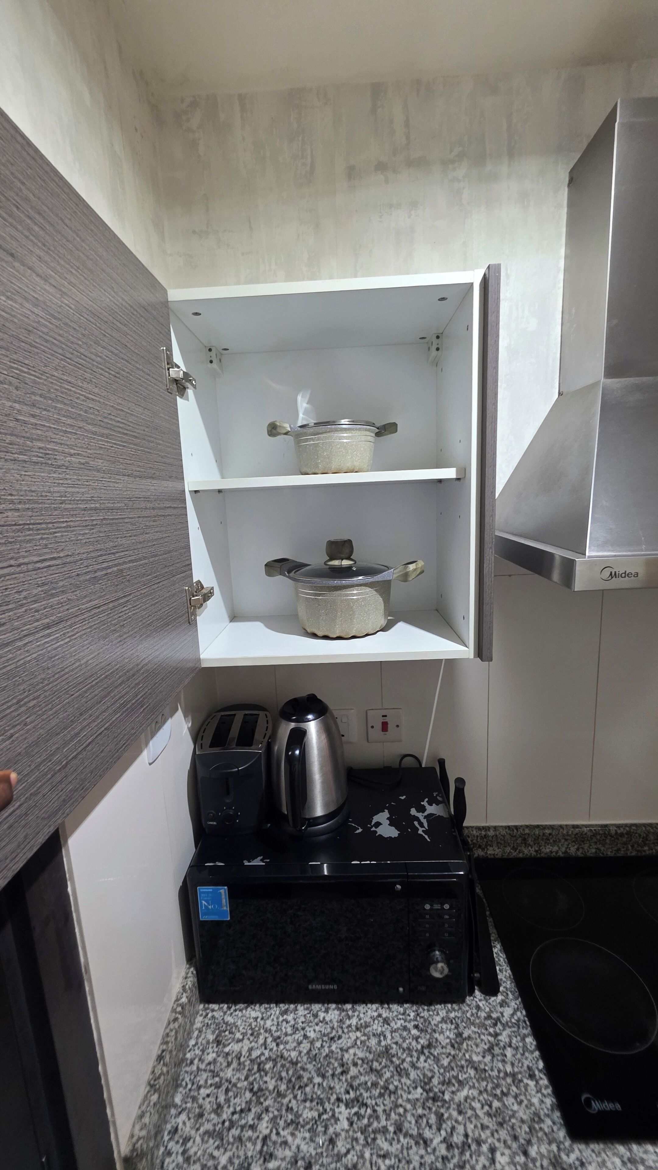Une cuisine compacte équipée d’un four encastré, d’un four à micro-ondes, d’une bouilloire et d’une casserole posée sur le plan de travail.