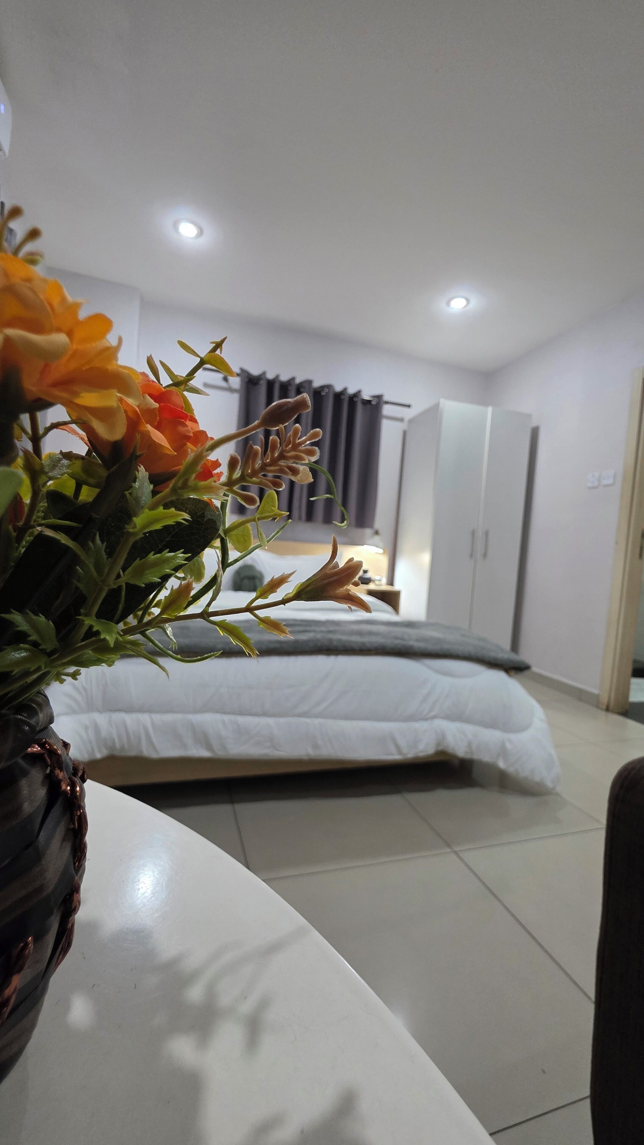 Ein Hotelzimmer mit einem Bett, einem Nachttisch mit Blumenvase, einem Kleiderschrank und einem Beistelltisch.