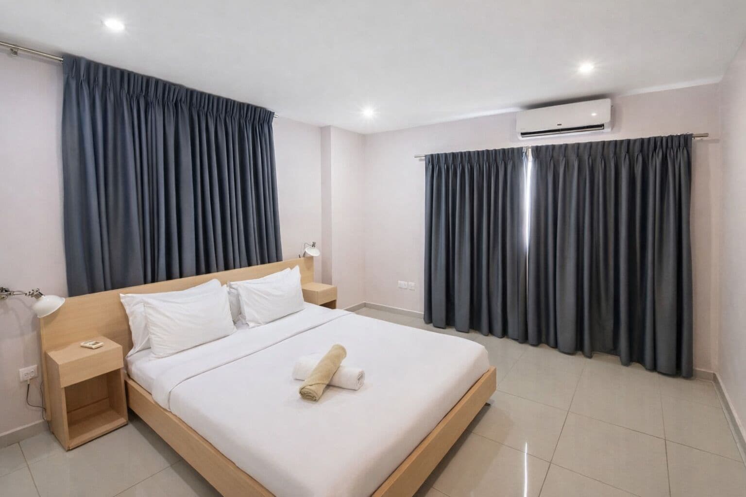 Ein Hotelzimmer mit einem großen Bett, zwei Nachttischen, einer Lampe und einem gefalteten Handtuch auf dem Bett.