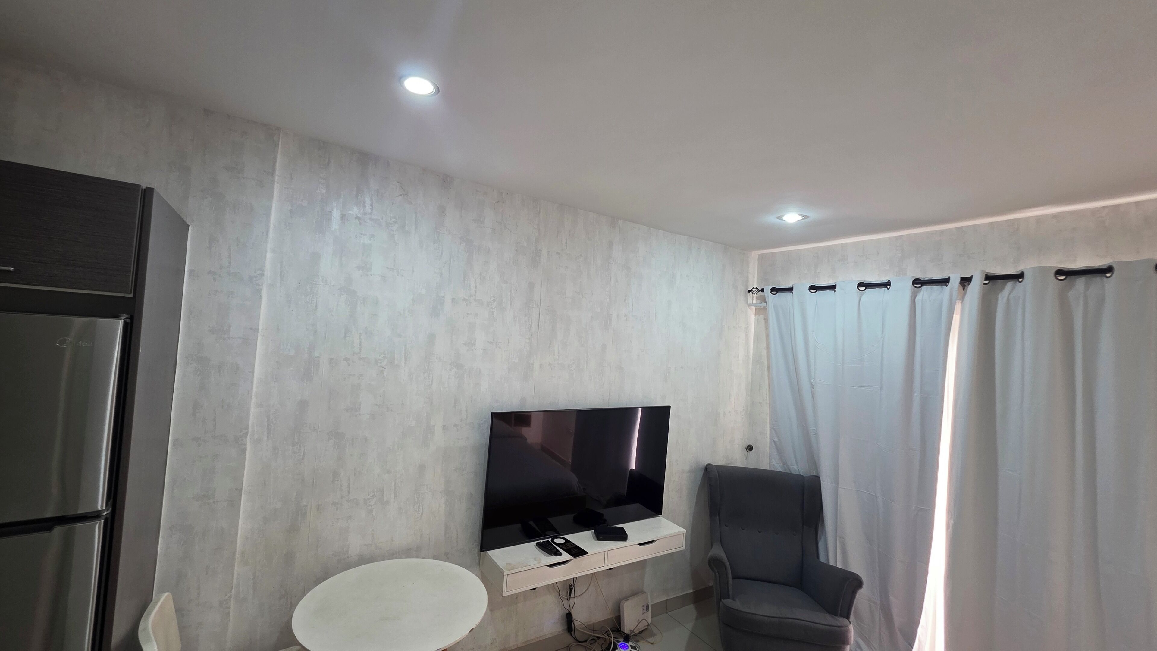 A modern living room with a flat-screen TV mounted on a wall, a grey armchair, a small white table, and a built-in cabinet.