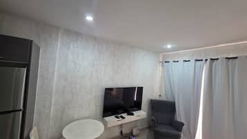 Een moderne woonkamer met een flatscreen televisie aan de wand, een grijze fauteuil, een klein wit tafeltje en een inbouwkast.