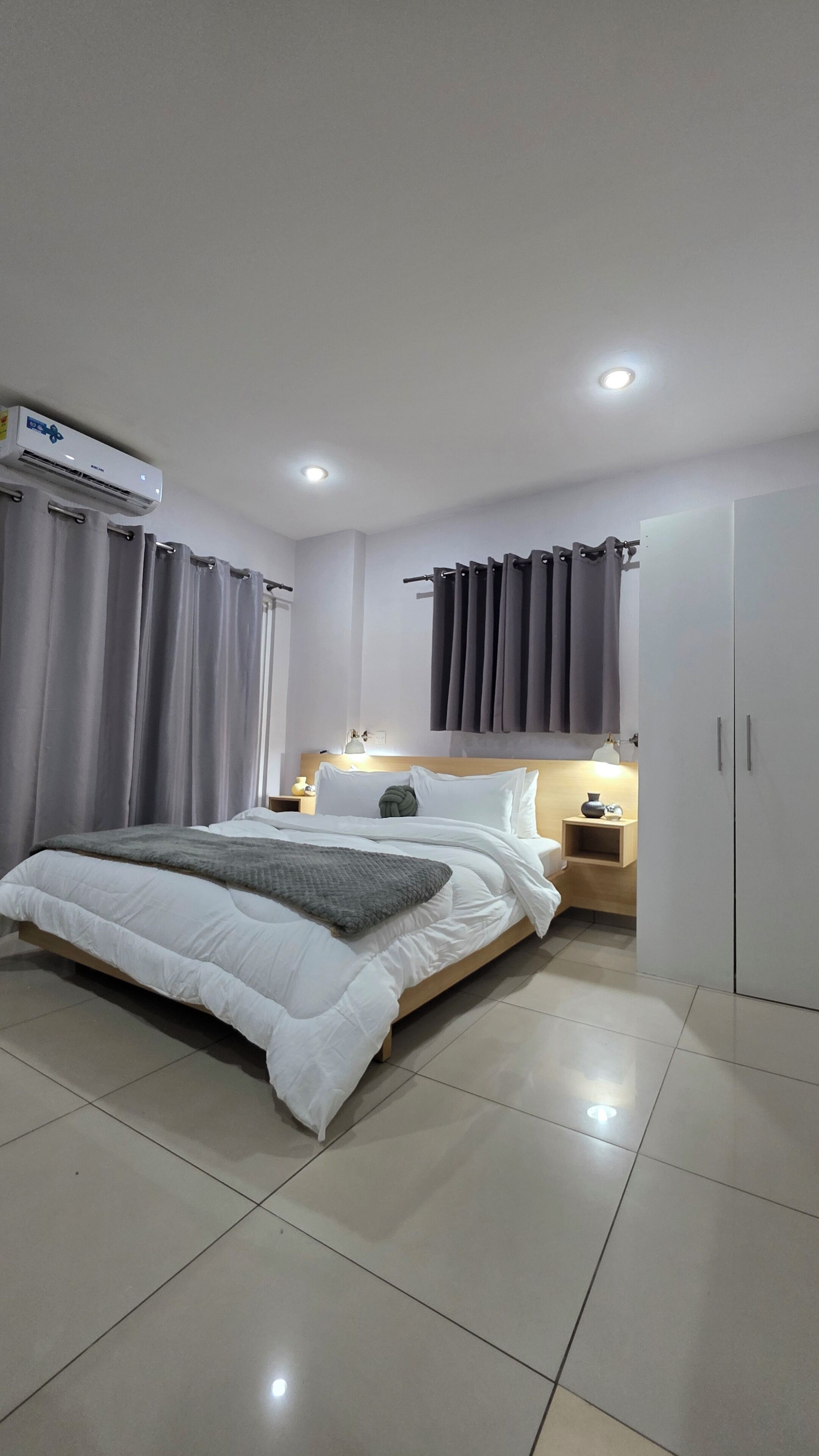 Un dormitorio moderno con una cama grande, una mesita de noche con lámpara, un armario y un equipo de aire acondicionado.