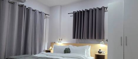 A modern bedroom with a large bed, a bedside table with a lamp, a wardrobe, and an air conditioning unit.