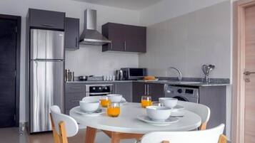 A modern kitchen with a dining table set for four, equipped with white chairs and bowls of orange juice.