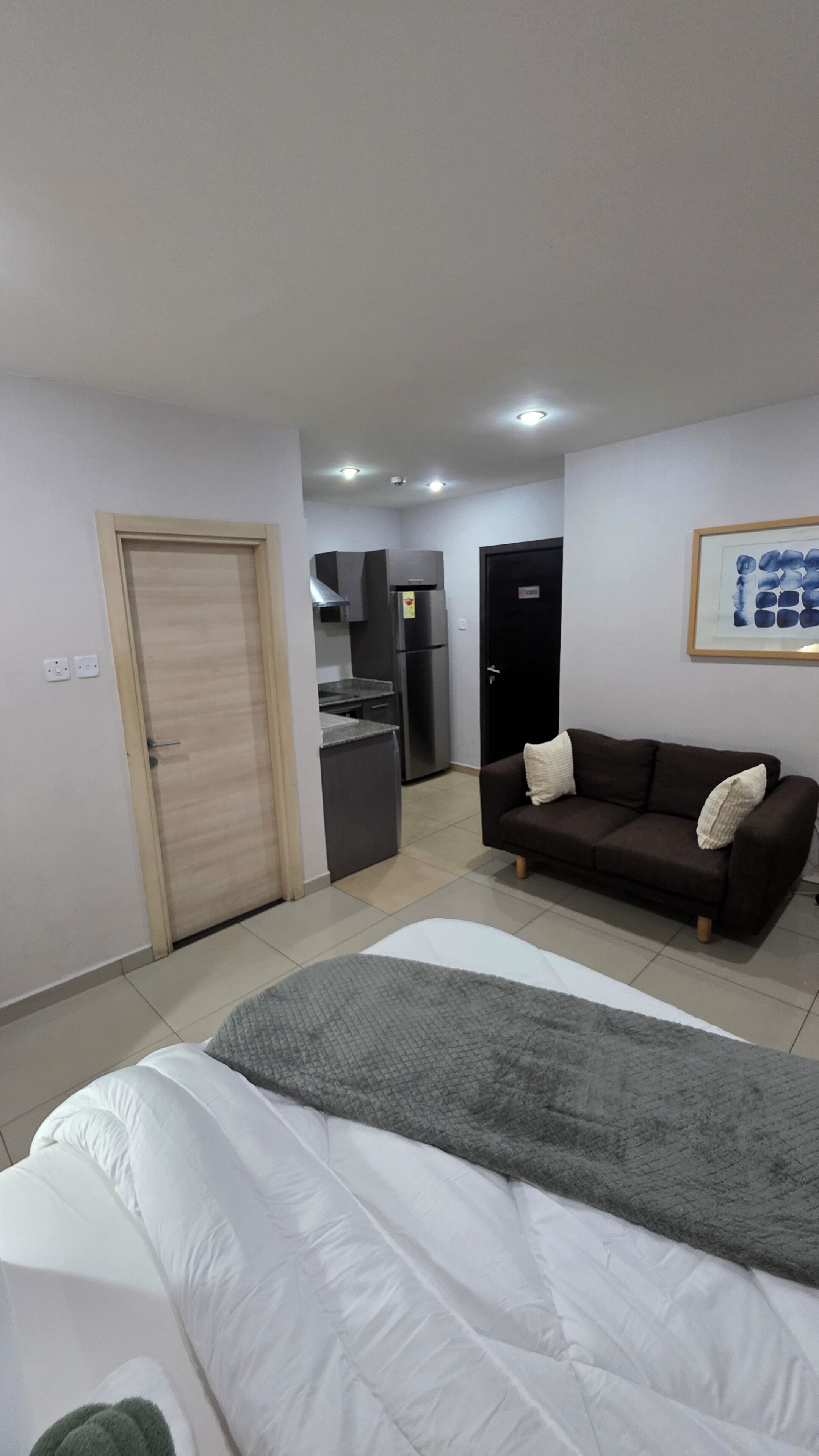 Een moderne hotelkamer met een bed, een bank, een kitchenette en een deur.