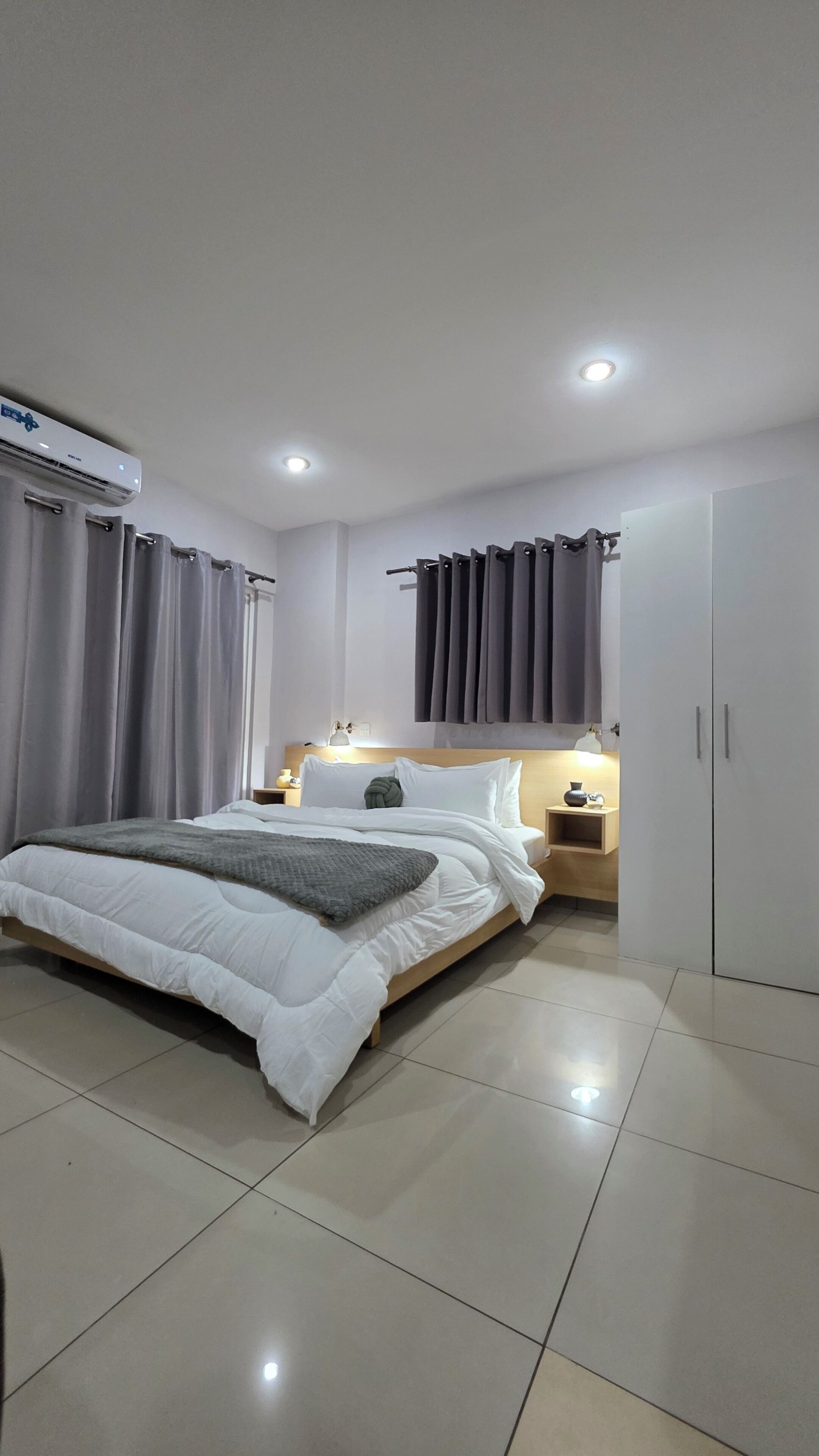 Un dormitorio moderno con una cama grande, una mesita de noche, un armario y un equipo de aire acondicionado.