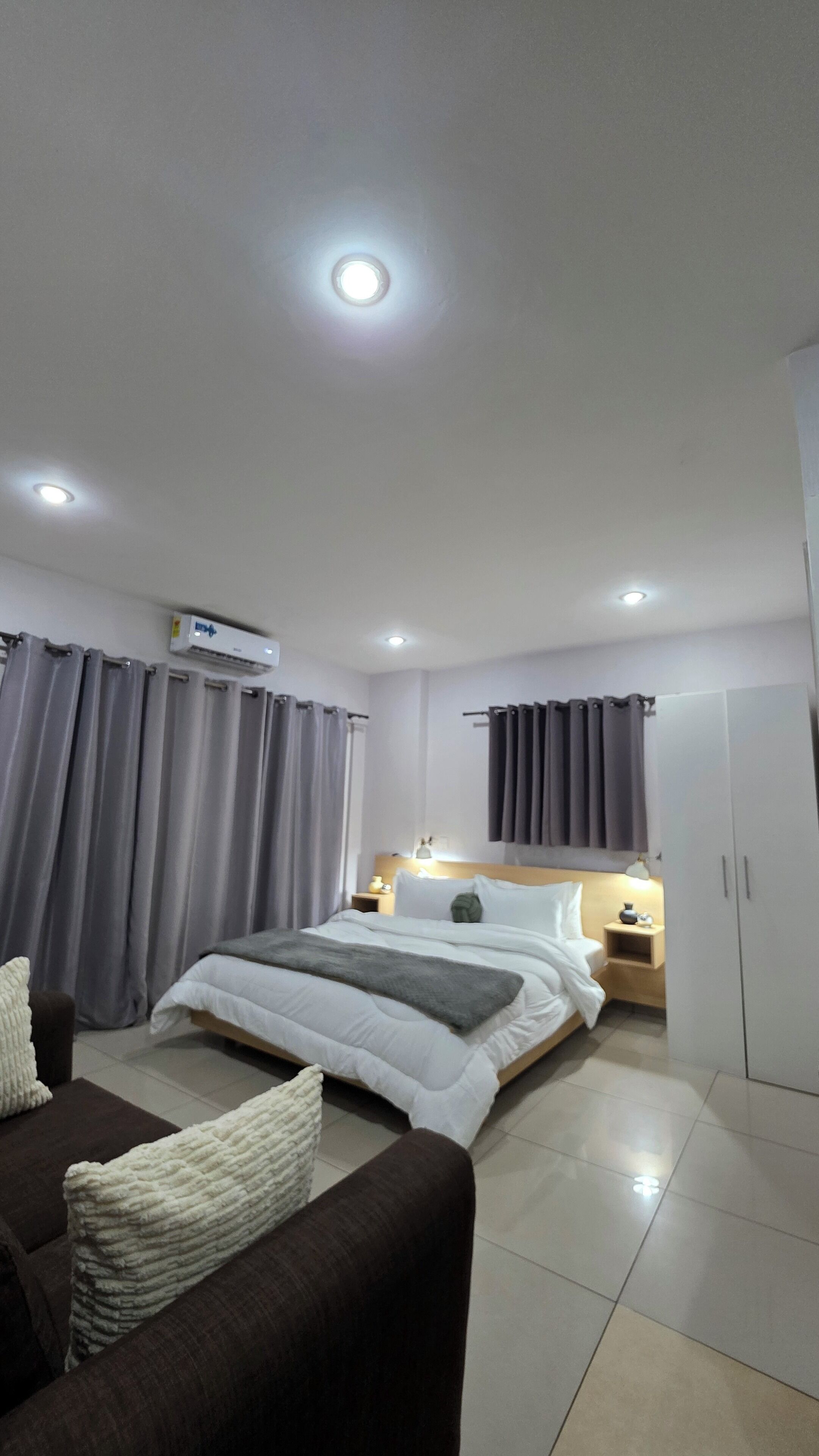 A modern hotel room with a large bed, a sofa, a nightstand, and a wardrobe.