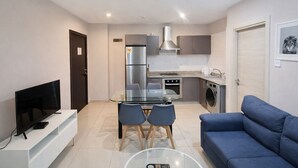 A modern apartment with a living room, dining area, kitchenette, and a TV on a white stand.