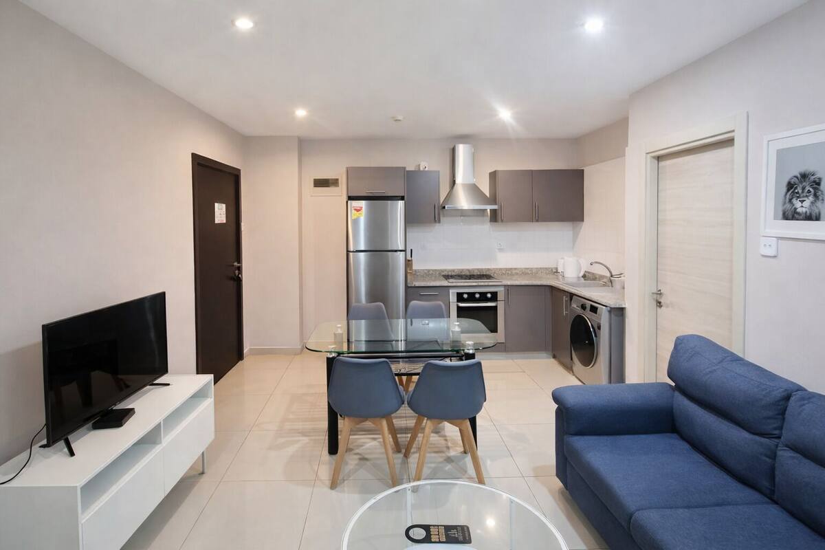A modern apartment with a living room, dining area, kitchenette, and a TV on a white stand.