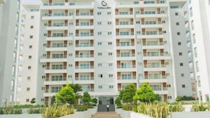 A multi-story residential building with a central entrance, surrounded by landscaped areas with benches.
