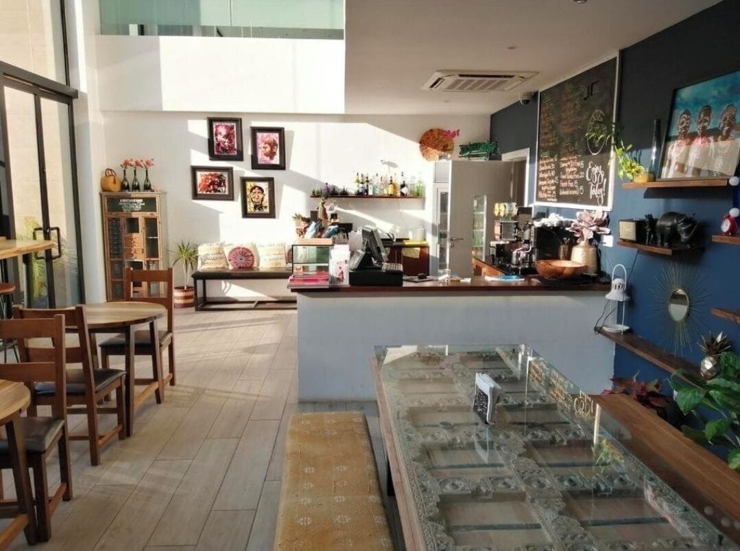 Un café acogedor con mobiliario de madera, una barra con caja registradora y diversas decoraciones, incluyendo cuadros enmarcados y plantas.