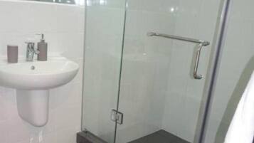 A bathroom with a glass shower enclosure, a pedestal sink, and a small rug on the floor.