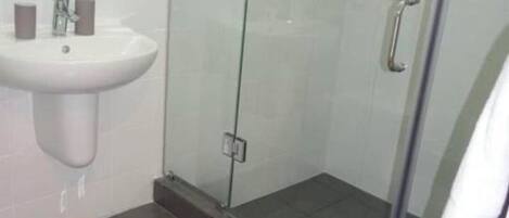 A bathroom with a glass shower enclosure, a pedestal sink, and a small rug on the floor.