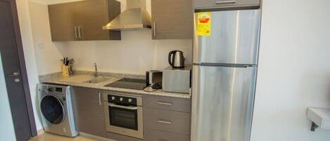 Una cocina moderna con electrodomésticos de acero inoxidable, horno empotrado, lavadora y cafetera.