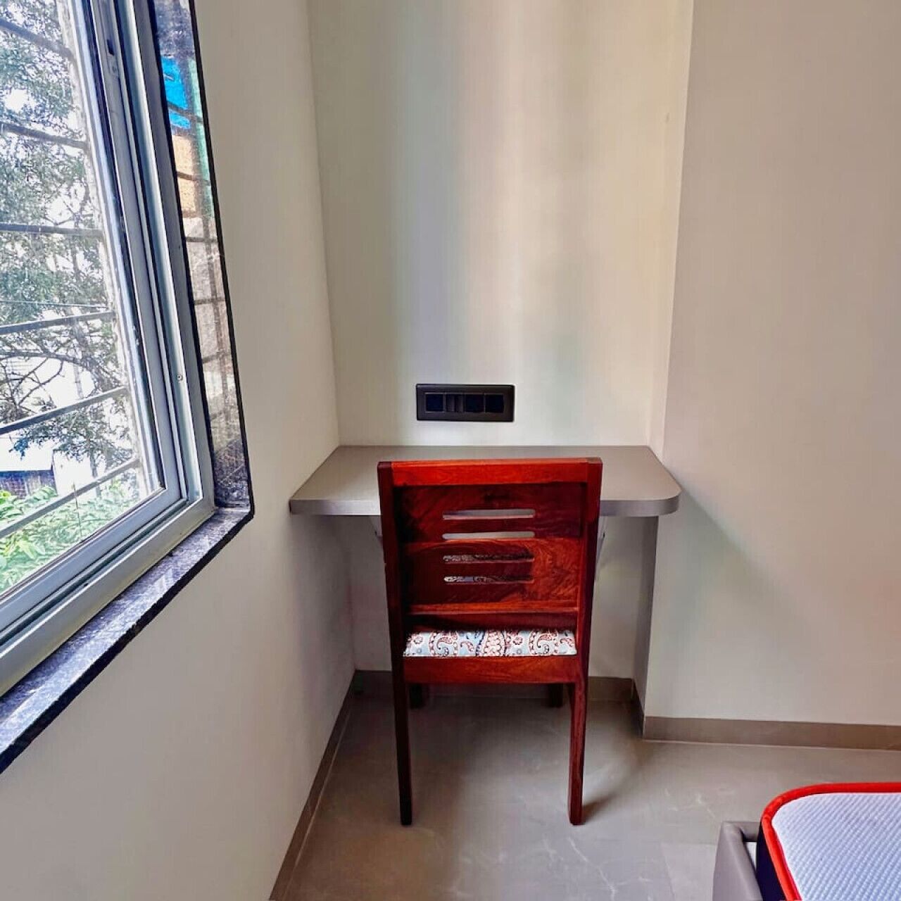 A corner room with a window, a desk, and a chair.