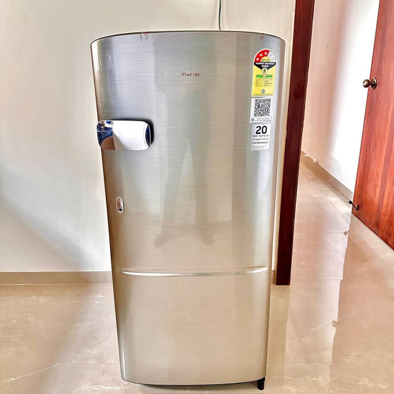 Un refrigerador de acero inoxidable con un asa, un código QR y una etiqueta que indica una garantía de 20 años.