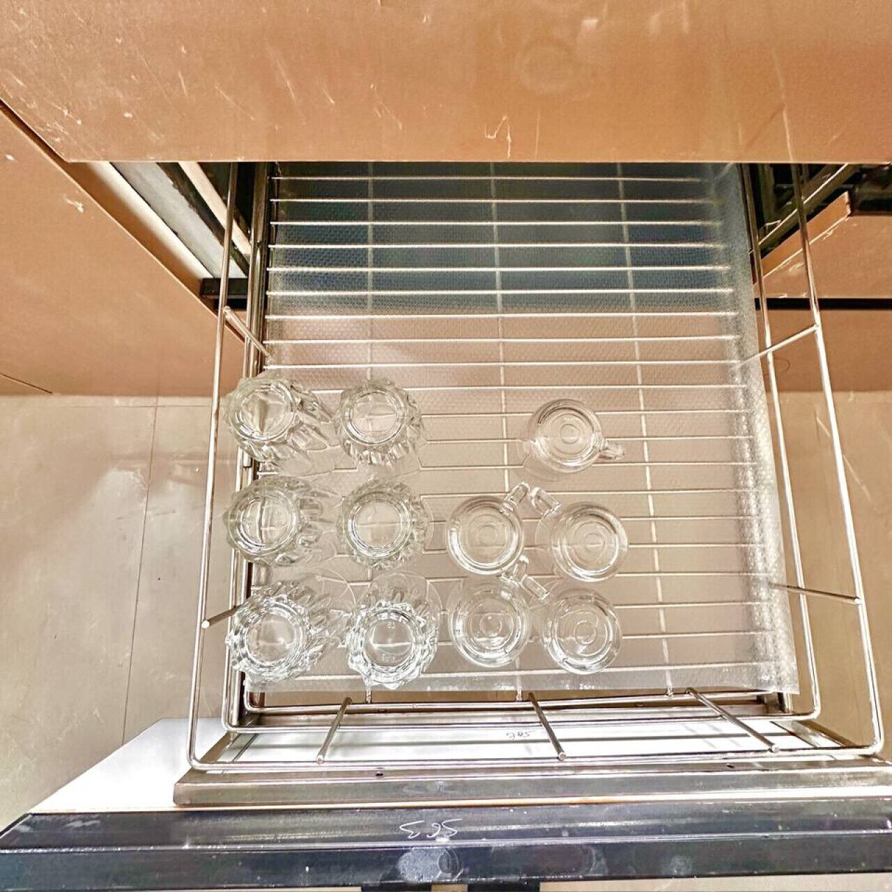 Una cocina con un estante que contiene varios vasos de vidrio transparentes.