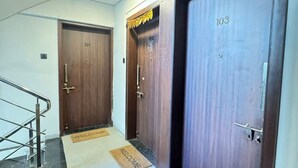 A hallway with two wooden doors, each marked with a number, and a metal staircase on the left. - Canary Haven: 2BHK Modern AC Flat in Pimple Nilakh (Pimpri-Chinchwad)