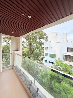 A balcony with a wooden ceiling, glass railing, and a view of surrounding buildings and greenery.