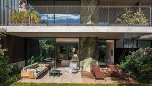Ein modernes Haus mit einer gläsernen Veranda, Gartenmöbeln und Blick ins Innere.