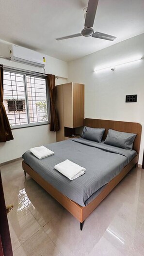 Une chambre à coucher avec un lit, un ventilateur de plafond, une fenêtre avec des rideaux et une armoire.