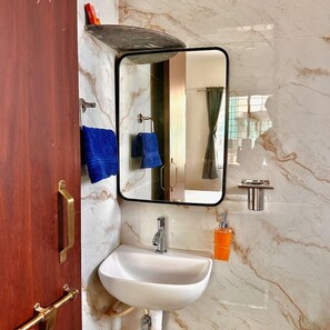 Une salle de bain avec un mur en marbre, un lavabo blanc, un miroir et un porte-serviettes.