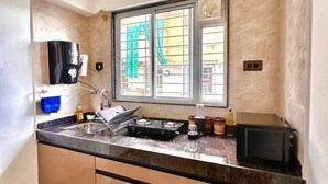 A compact kitchen with a built-in stove, a coffee machine, and a window with a view of the outside. - Crane House: Spacious 2BHK AC Flat by Bleisure (Pimpri-Chinchwad)