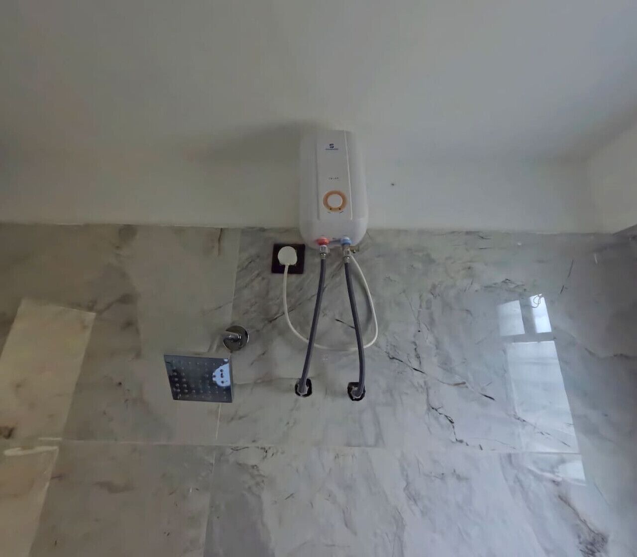 Een warmwaterboiler op een betegelde vloer, met een bedieningspaneel en een apart thermostaat.
