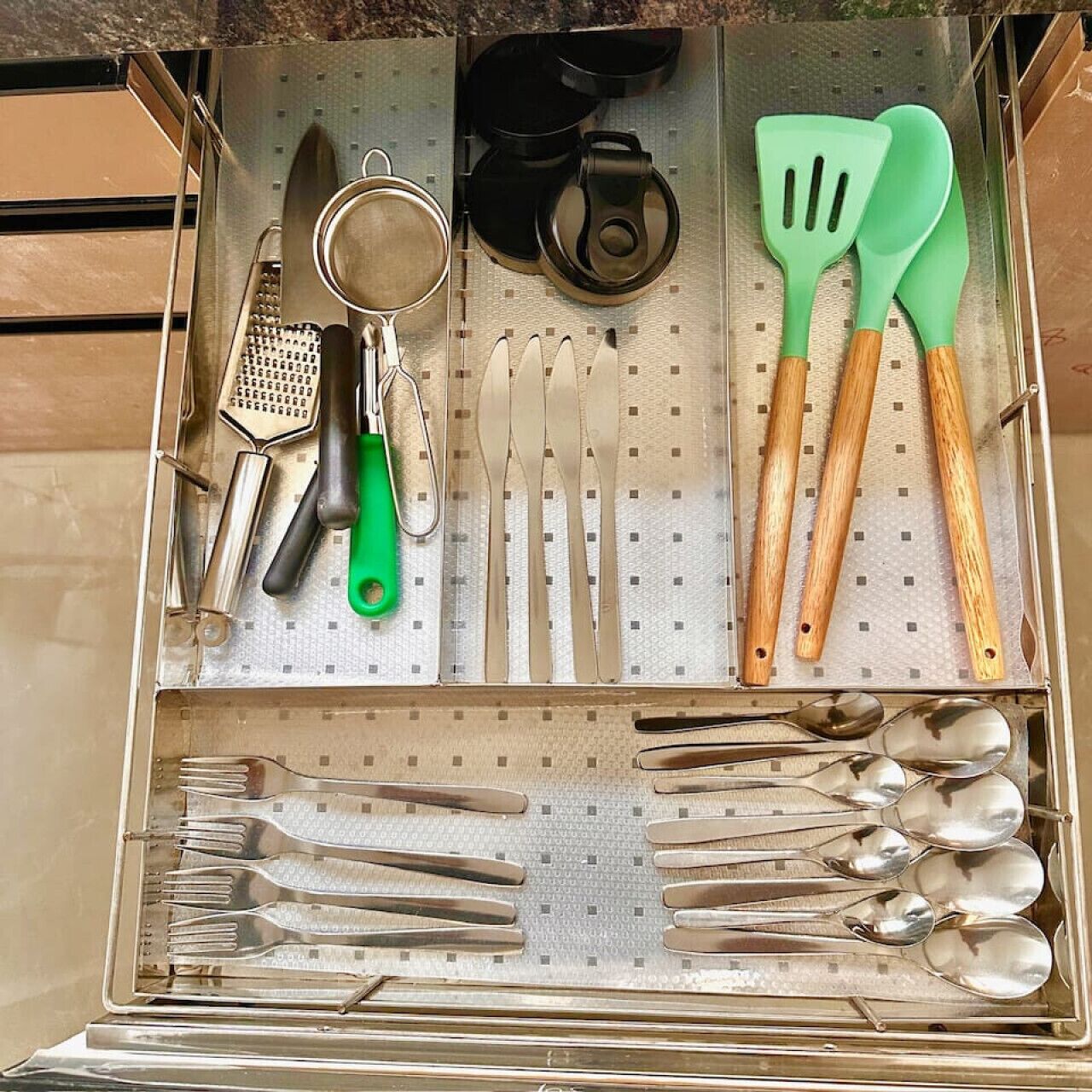A drawer with kitchen utensils including a grater, spatulas, and various spoons and forks.
