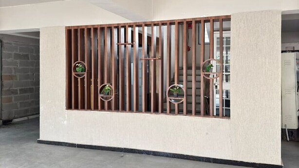 A spacious room with a high ceiling, a concrete floor, and a partition with vertical slats and circular windows. - Crane House: Spacious 2BHK AC Flat by Bleisure (Pimpri-Chinchwad)