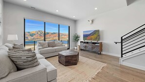 Een ruime woonkamer met een groot raam dat uitzicht biedt op een schilderachtig berglandschap, een moderne trap en een minimalistisch design.
