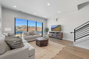 Ein geräumiges Wohnzimmer mit großem Fenster und weiter Aussicht auf die Berge, einer modernen Treppe und einem minimalistischen Design.