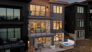 Een modern meerlaags huis met balkon, jacuzzi en een gevel van natuursteen.