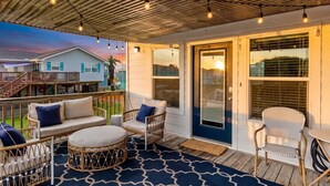 A covered outdoor area with wicker furniture, a patterned rug, and string lights. - Cozy Coastal Home, Minutes from the Beach (Jamaica Beach)
