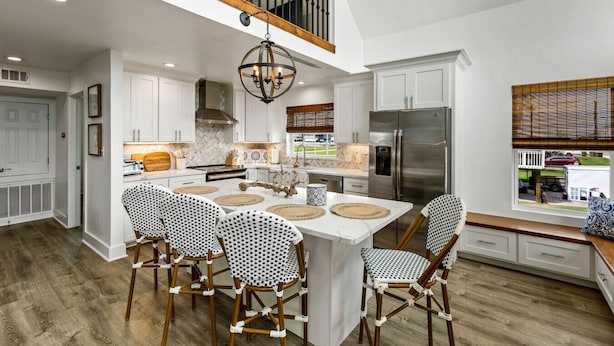A spacious kitchen with white cabinets, a stainless steel refrigerator, and a wooden dining table with four chairs. - Cozy Coastal Home, Minutes from the Beach (Jamaica Beach)