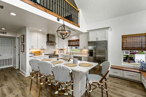 Una cocina amplia con armarios blancos, un refrigerador de acero inoxidable y una mesa de madera con cuatro sillas.