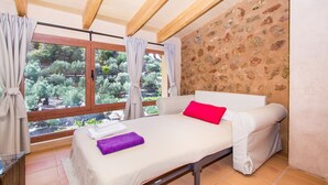 Une pièce avec un lit, une fenêtre avec des rideaux, un mur en pierre et une vue sur les arbres.