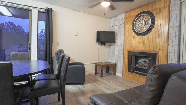 A living room with a wooden wall, a fireplace, a TV mounted on the wall, and a dining area with a table and chairs. - Quaint 1-bedroom condo is perfect for relaxing 101 - Lava Hot Springs Resort (Lava Hot Springs)