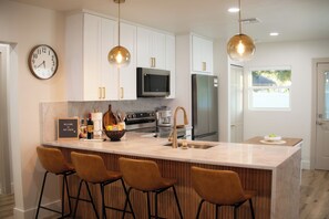 A modern kitchen with white cabinets, a central island with stools, stainless steel appliances, and pendant lighting. - Cozy 2-bedroom casita, EV Charger, No cleaning fees. (Seffner)