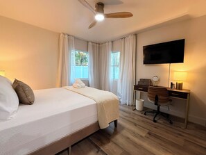 A hotel room with a bed, desk, chair, TV, and curtains. - Cozy 2-bedroom casita, EV Charger, No cleaning fees. (Seffner)