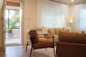 A living room with a sofa, armchair, and floor lamp. - Cozy 2-bedroom casita, EV Charger, No cleaning fees. (Seffner)
