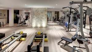 A modern gym with various exercise equipment, a stone wall feature, and a wooden floor.